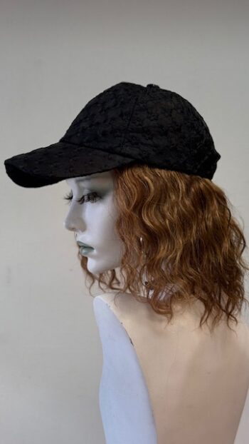 A mannequin wearing a black hat with a curly hair style.