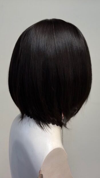 A black haired woman with long hair in front of a white wall.