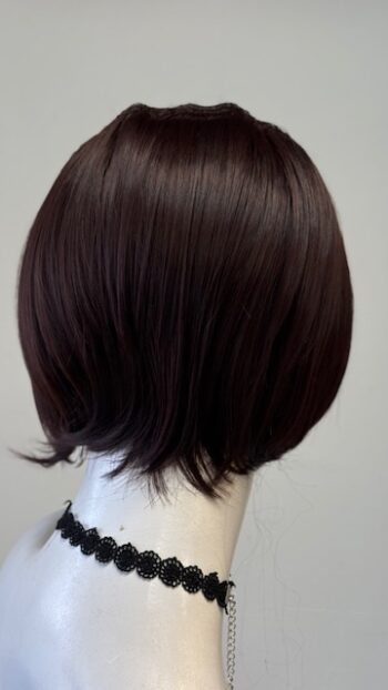 A woman 's head with dark brown hair in front of a white wall.